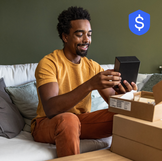 A Black man sits on a sofa, smiling while unboxing his eBay order. Links to Money Back Guarantee page.