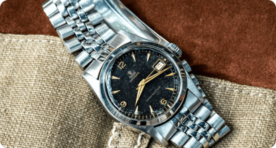 Tudor watch on a piece of fabric on a wooden table.