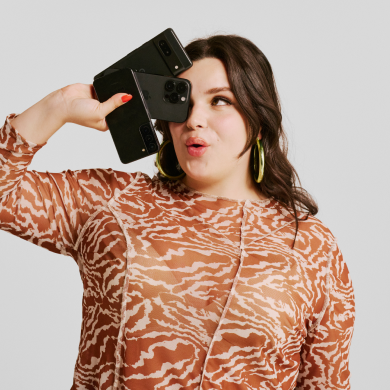 A pleased-looking woman holds several smartphones close to her face. Image links to Electronics page.