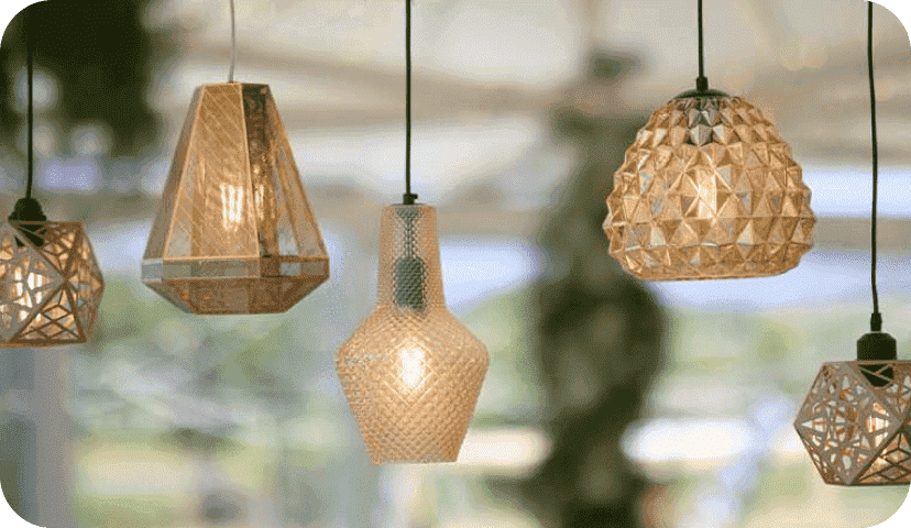Five hanging pendant lights against a blurred outdoorsy background. The lamps vary in geometric shapes and materials; the first and the fifth lamps are made of wood, the second lamp is made of steel, and the third and fourth are made of glass.