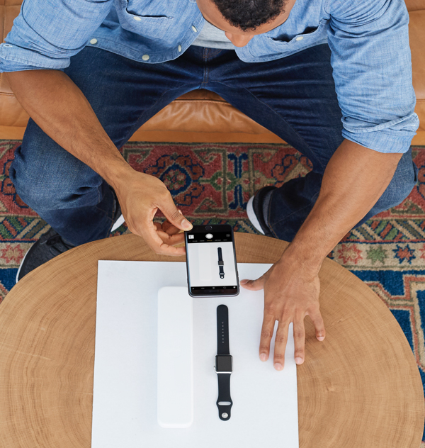 Image of a man taking a photo with his phone of a watch that's laid out on a sheet of paper.