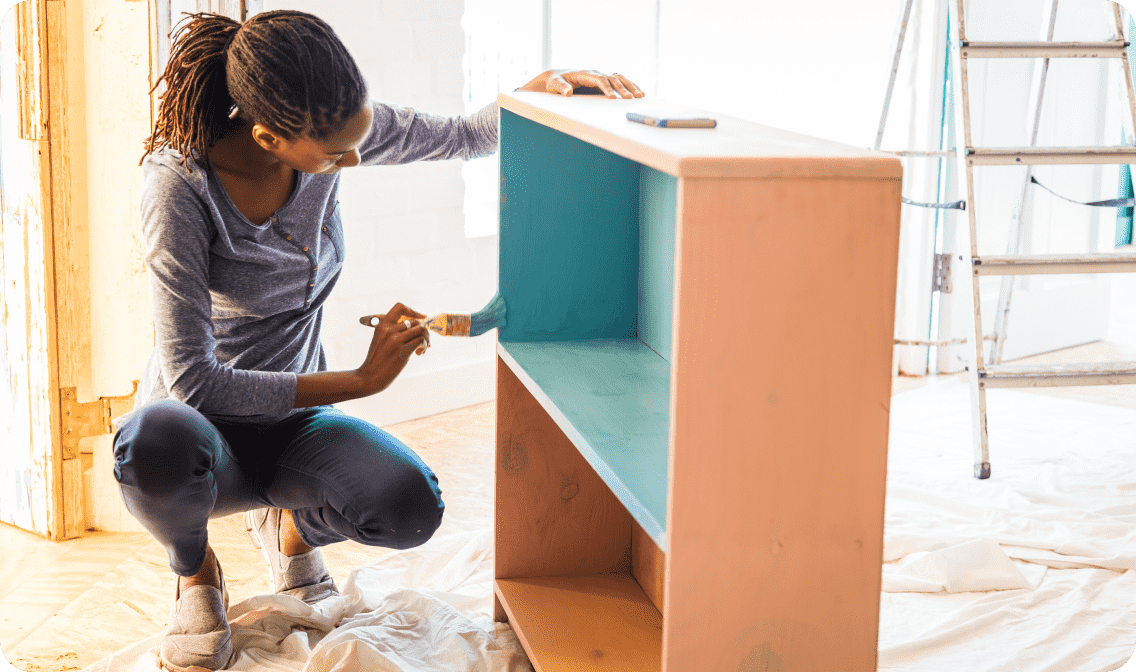 A person holding a paint brush with blue paint against a bookshelf