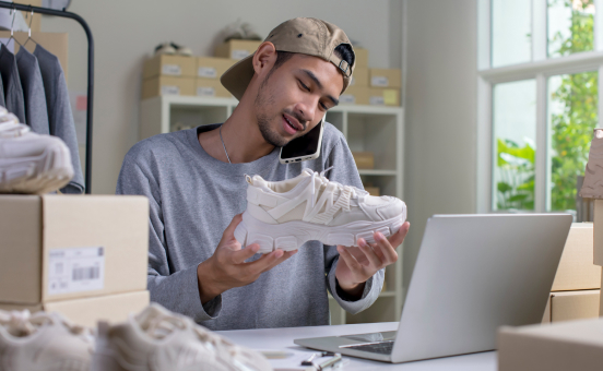 A man in a baseball cap examines a white athletic shoe. Links to Selling page.