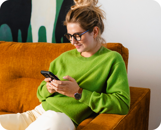 Woman sitting on a couch, holding a smartphone while smiling