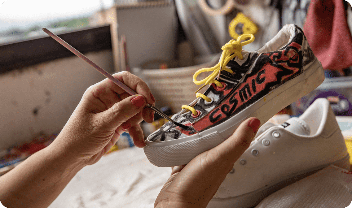 A person painting white sneakers with the word cosmic linking to DIY landing page
