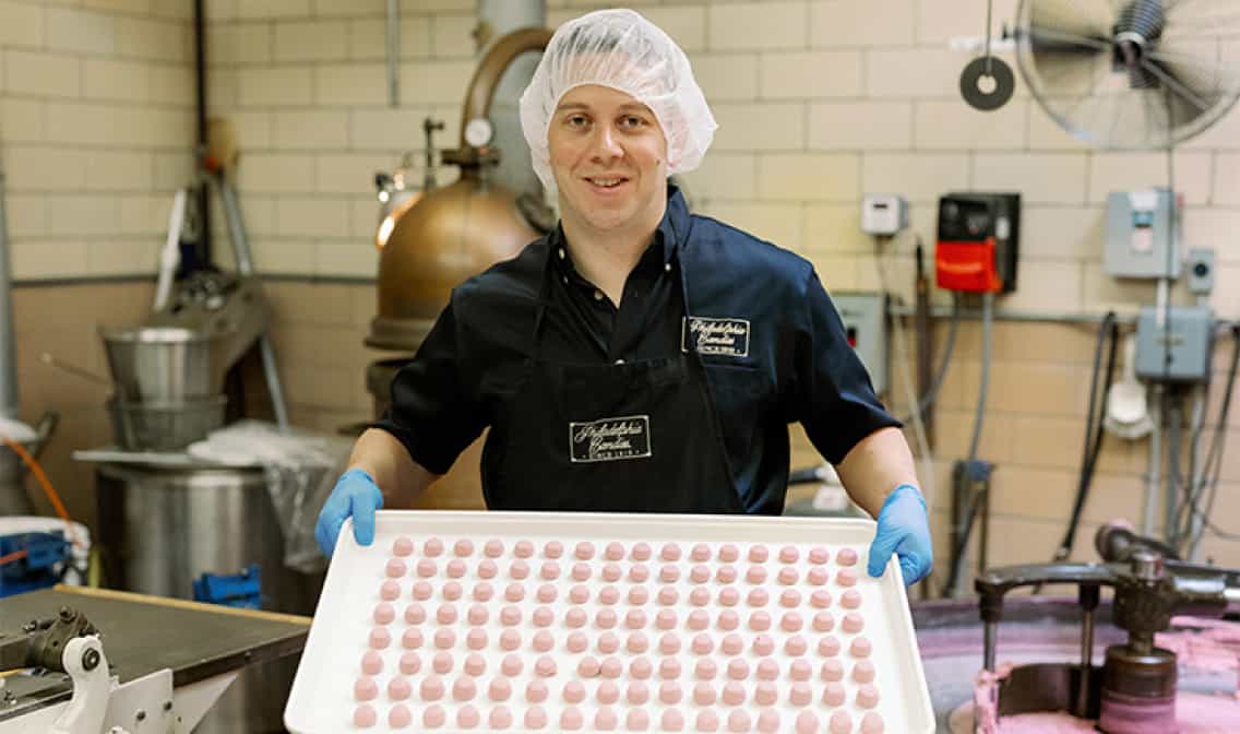 A man holding a tray of pink chocolates linking to Philadelphia Candies eBay store