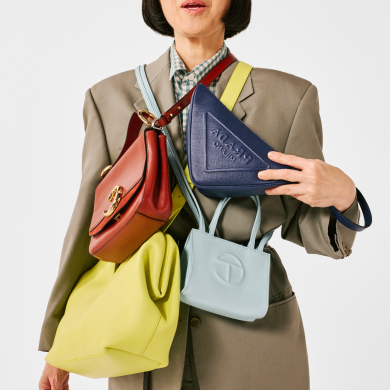 Image shows woman draped with colorful luxury handbags. Links to Brand Outlet page.