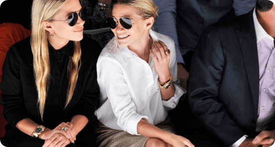 Two women in sunglasses sitting next to each other smiling.