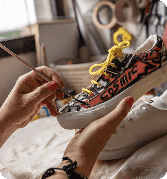 A person painting white sneakers with the word cosmic linking to DIY landing page