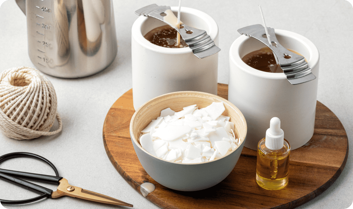 Candle wicks in molds with wax, a dropper with yellow liquid, scissors, and a ball of yarn