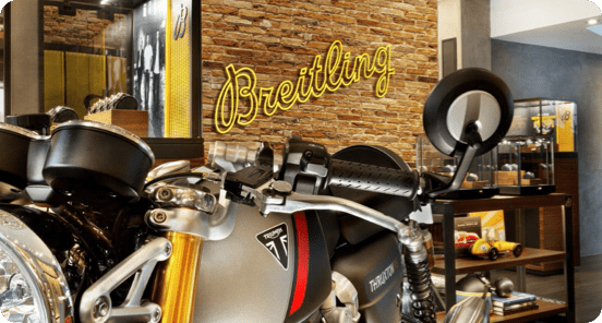 Motorcycle inside an office-like setting with a yellow 'Breitling' sign in the background.