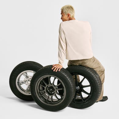 A man sits on a trio of car tires with his back facing the camera. Links to US Motors page.