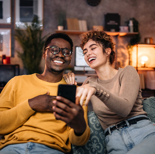 Two people laughing and browsing on a smartphone, linking to downloading the app.