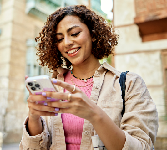 A young woman with curly brown hair smiles while looking at her smartphone. Links to app download page.